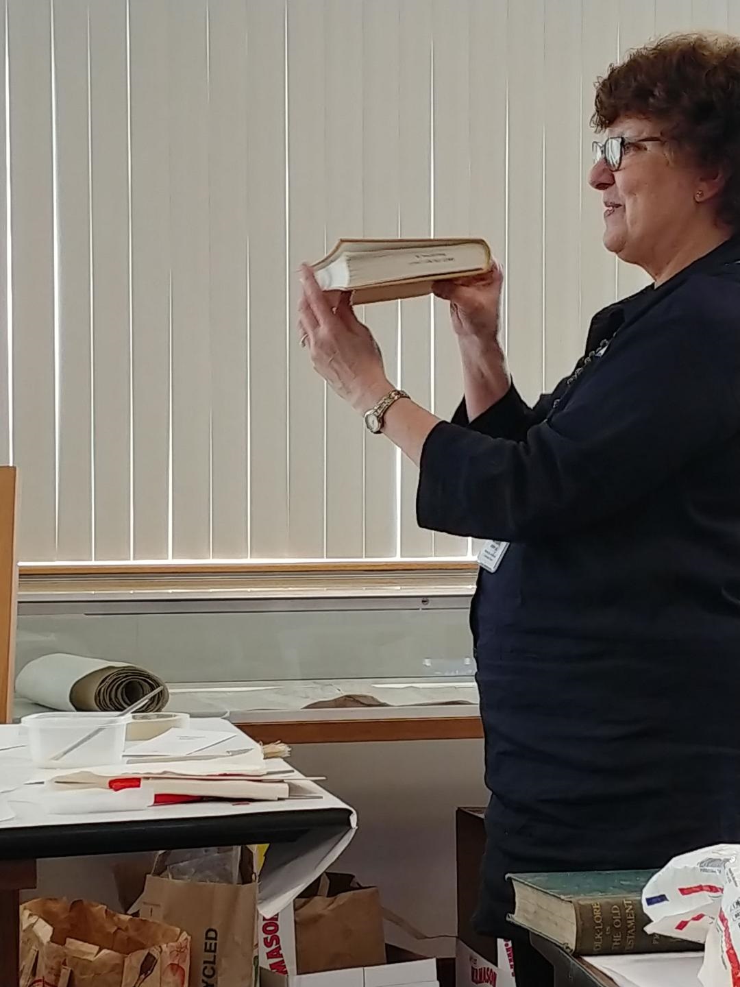 A woman with glasses holds a torn book at eye level.